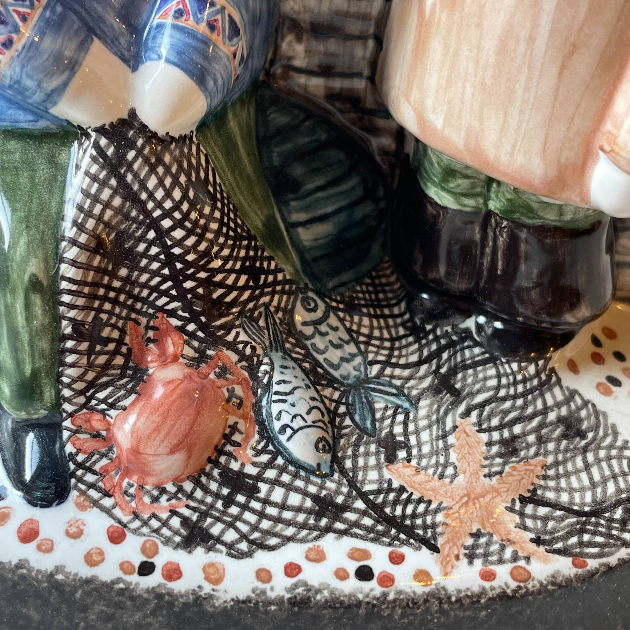 Detail from hand made ceramic figure depicting sussex fisherman mending their nets with fish and shell fish in the nets