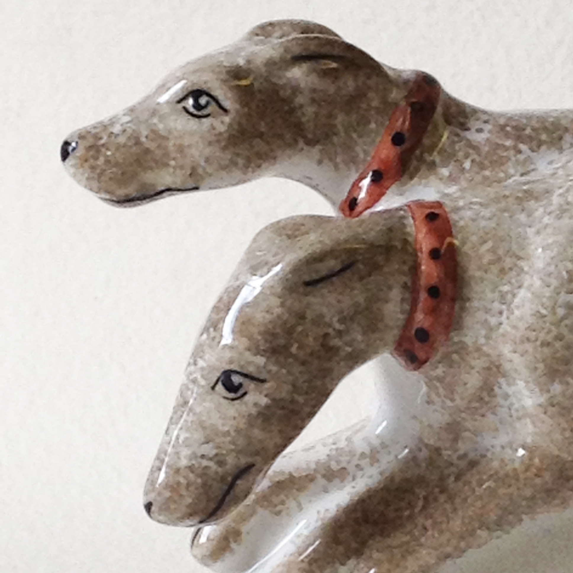 Close up detail of the faces of hand made ceramic hounds figurine sculpture showing two dogs on the opposite side